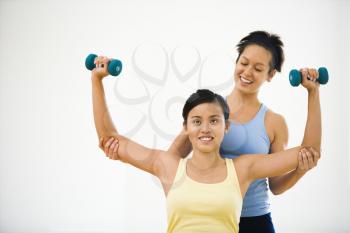 Royalty Free Photo of a Woman Lifting Weights While Another Woman Helps Position Her Arms