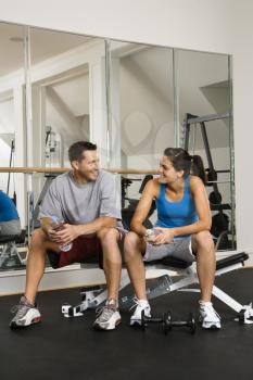 Royalty Free Photo of a Man and Woman Sitting on an Exercise Machine Talking Holding Water Bottles