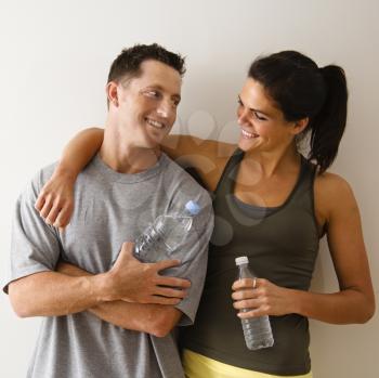 Royalty Free Photo of Man and Woman at a Gym in Fitness Attire Holding Water Bottles Smiling at Each Other
