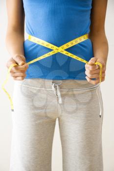 Woman standing pulling measuring tape around waist.