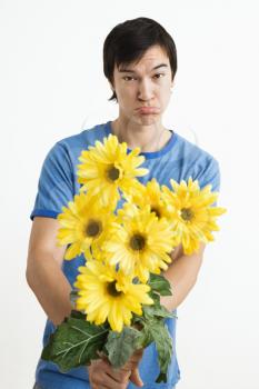 Royalty Free Photo of a Young Man Holding a Bouquet of Yellow Gerber Daisies While Pouting