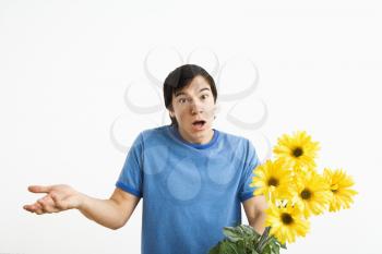 Royalty Free Photo of a Man Holding a Bouquet of Yellow Gerber Daisies Shrugging