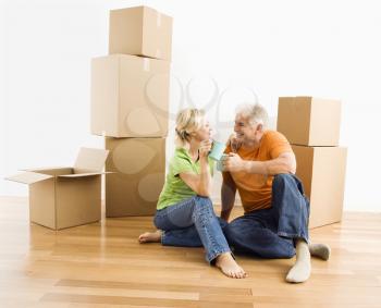 Royalty Free Photo of a Middle-aged Couple Sitting on a Floor Among Cardboard Moving Boxes Drinking Coffee