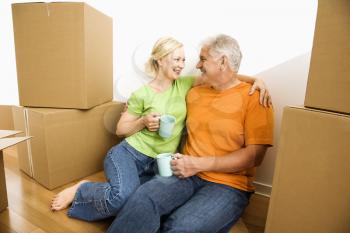 Royalty Free Photo of a Middle-aged Couple Sitting on a Floor Among Cardboard Moving Boxes Drinking Coffee