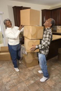 Smiling senior african american man balancing moving boxes while his wife helps. Vertical shot.