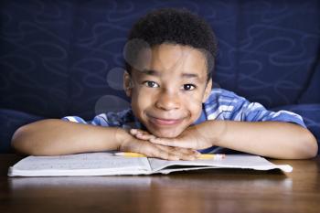 Young African American boy sitting on the floor in front of a coffee table with his homework. He smiles towards the camera. Horizontal shot.