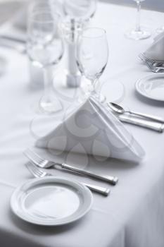 Place settings on an elegant, white dining table in a restaurant. Vertical shot.