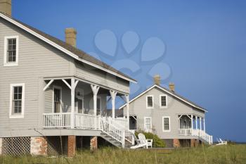 Cropped, low angle view of two identical looking beachfront homes against a backdrop of a clear, blue sky. Horizontal shot.