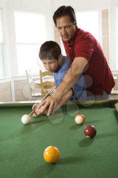 Man shooting game of pool with young boy.  Vertically framed shot.