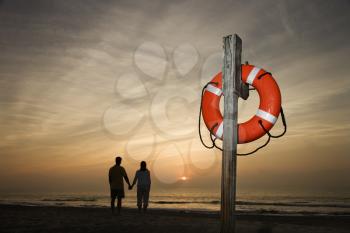 Silhouette of couple holding hands on beach watching the sunset with life preserver in foreground