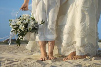 Bride and flower girl stand on a sandy beach. Horizontal shot.