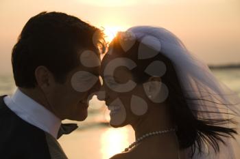 Newlyweds with their heads together in front of a setting sun on the beach. Horizontal shot.