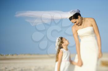 Bride and a flower girl look at each other on a sandy beach. Horizontal shot.