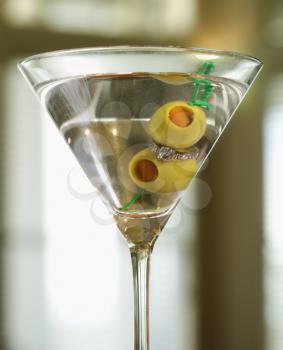 Closeup of a martini glass with an engagement ring amongst the olives. Vertical shot.