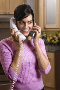 Smiling woman multitasks between her cell phone and landline telephones. Vertical shot.