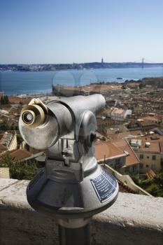 Pay telescope overlooking homes and buildings in the city with bridge and waterway in the background. Vertical shot.