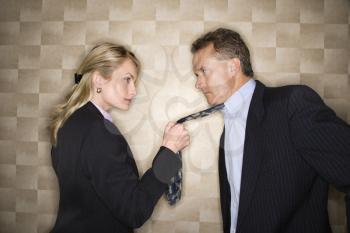 Caucasian mid-adult businesswoman staring into eyes of a middle-aged businessman while pulling on his tie. Horizontal format.