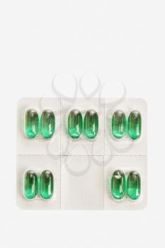 Green capsule tablets in an individual dose package. Vertical shot. Isolated on white