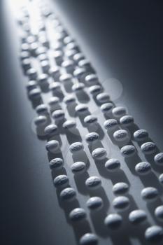 White round pills illuminated by a shaft of light. Vertical shot.