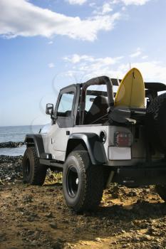 SUV parked on a rocky beach with a surfboard sticking out of the back seat. Vertical format.