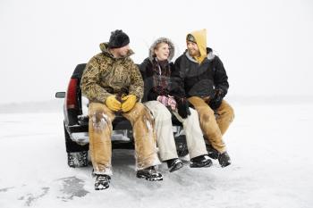 Two young men and a young woman having a beer while sitting on the tailgate of a truck in a winter environment. Horizontal shot.