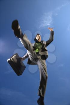 Young businessman leaps over the viewer with a briefcase in hand. Vertical shot.