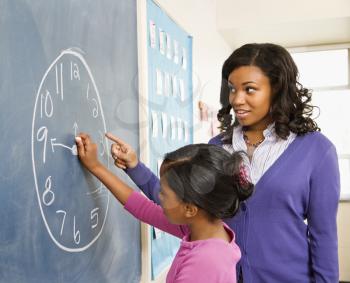 Teacher and female student at the blackboard with clock drawing on it.