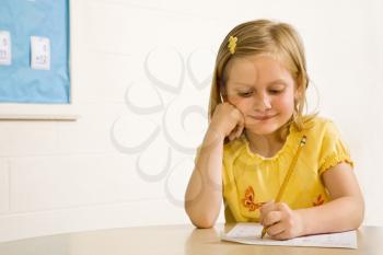 Young girl smiling in classroom writing on paper. Horizontally framed shot.