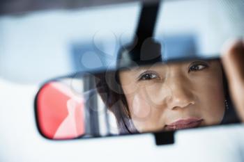 Reflection of Asian woman in rearview car mirror.