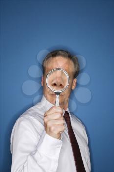 Caucasian middle aged businessman looking through magnifying glass.