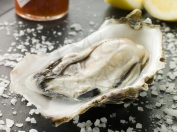 Royalty Free Photo of Opened Rock Oyster with Hot Chili Sauce Lemon and Sea Salt