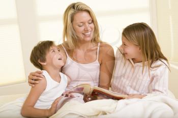 Royalty Free Photo of a Woman in Bed Reading to Her Children