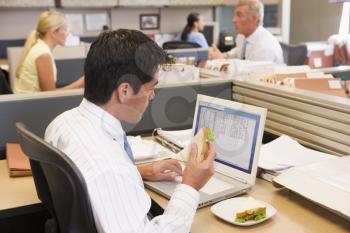 Royalty Free Photo of a Man in an Office Cubicle Eating a Sandwich