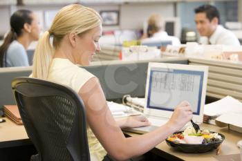 Royalty Free Photo of a Woman Eating a Salad in an Office Cubicle