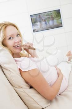 Royalty Free Photo of a Pregnant Woman in Front of the TV Eating Chocolate