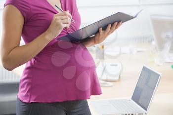 Royalty Free Photo of a Pregnant Woman With a Binder Beside a Laptop