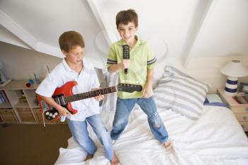 Royalty Free Photo of Two Boys Playing Guitar and Singing While Standing on a Bed