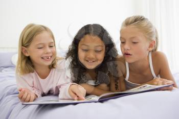 Royalty Free Photo of Three Girls Lying on a Bed Reading a Story