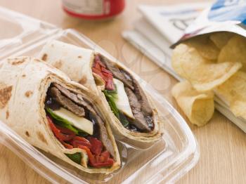 Royalty Free Photo of a Steak, Cheese, Red Pepper And Barbecue Sauce Tortilla Wrap With A Can Of Cola And Packet Of Crisps