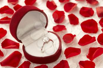 Royalty Free Photo of a Diamond Ring in a Heart Shaped Box Surrounded by Rose Petals