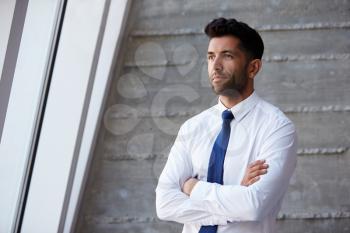Hispanic Businessman Standing Against Wall In Modern Office