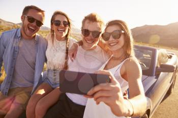 Friends On Road Trip Sit On Convertible Car Taking Selfie