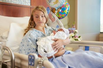 Unhappy Teenage Girl Holding Newborn Baby Son In Hospital