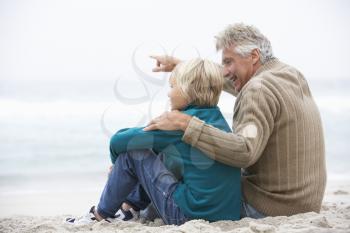 Grandfather And Son Sitting On Winter Beach Together