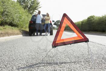 Couple Broken Down On Country Road With Hazard Warning Sign In Foreground