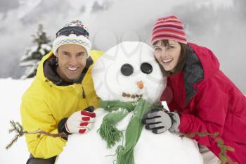 Middle Aged Couple Building Snowman On Ski Holiday In Mountains