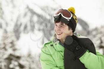 Teenage Boy With Snowboard On Ski Holiday In Mountains