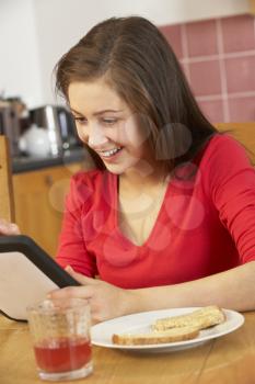 Teenage Girl Using Tablet Computer Whilst Eating Breakfast