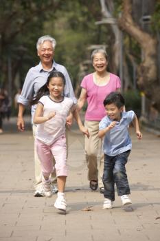 Chinese Grandparents Walking Through Park With Running Grandchildren