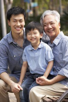 Male Multi Genenration Chinese Family Group Sitting On Bench In Park Together